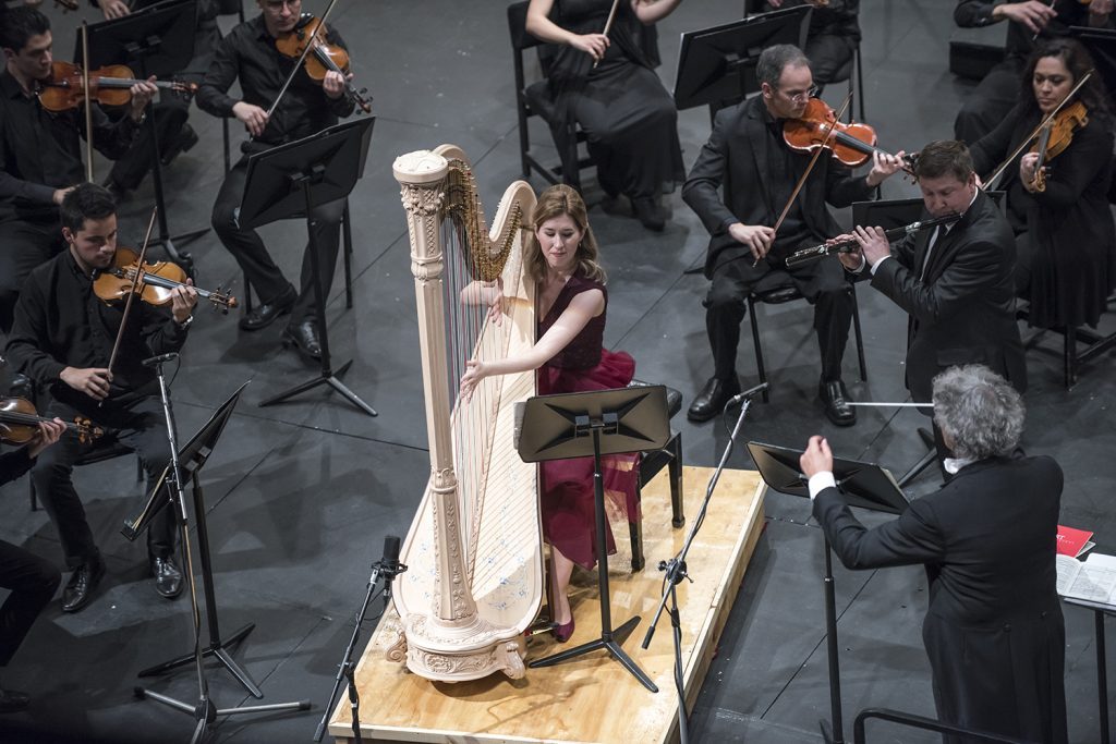 Orquesta sinfónica en concierto con arpista solista en primer plano durante presentación del Ceac Universidad de Chile