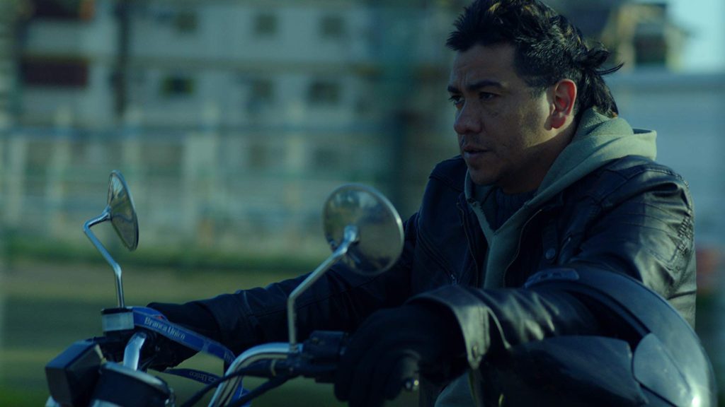 "El motoarrebatador", de Agustín Toscano: El filme que ganó la competencia internacional de SANFIC 14 Hombre con chaqueta azul sostiene un casco de motocicleta en las manos, fondo urbano desenfocado