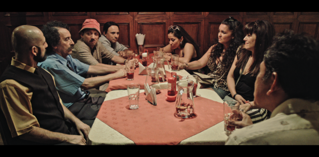 Grupo de personas alrededor de mesa redonda en interior cálido, escena de tensión social y encuentro urbano