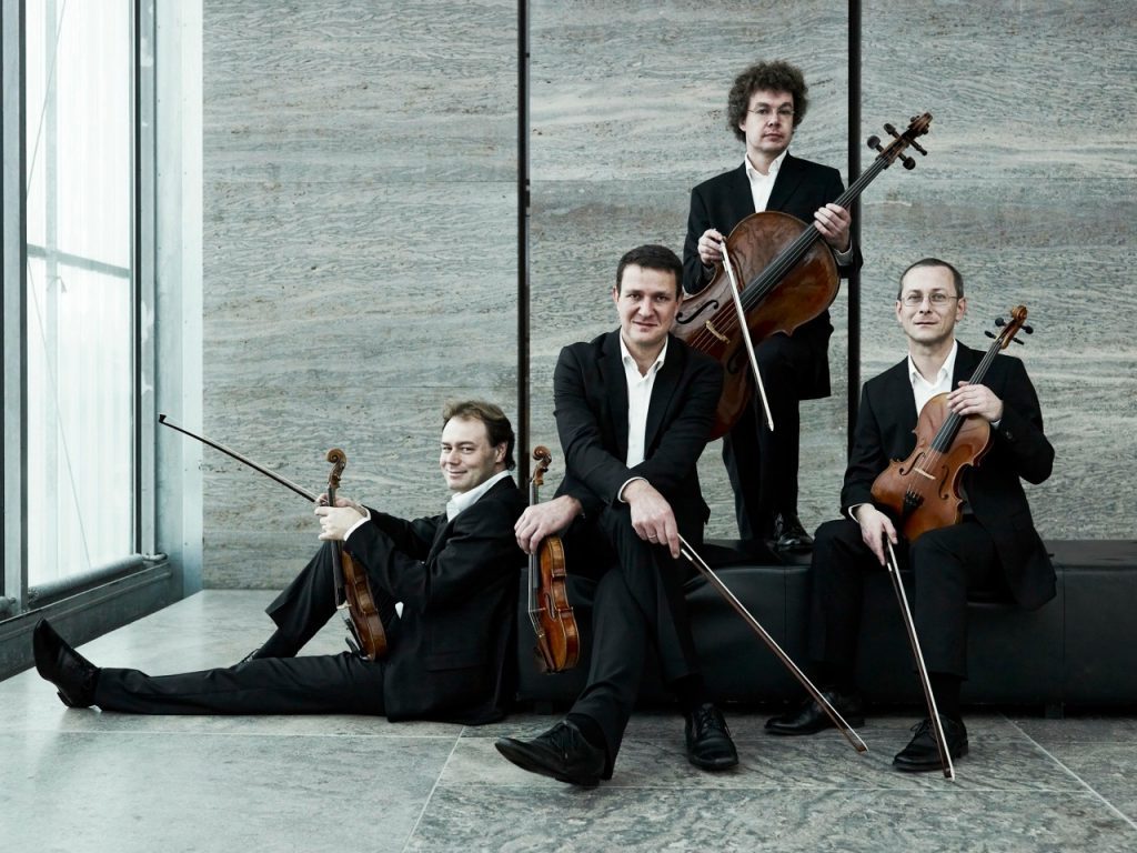 Cuarteto Leipzig en posición de concierto: cuatro músicos con instrumentos de cuerda en traje negro ante pared