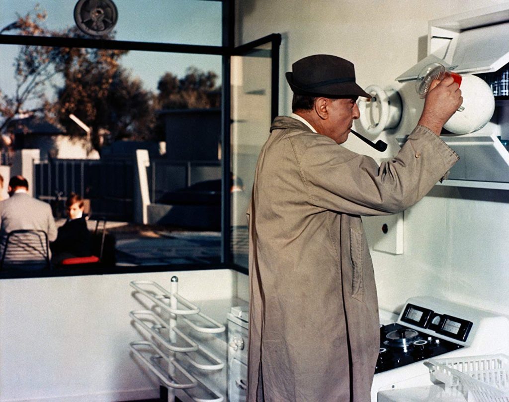 Jacques Tati ajusta una lámpara en interior minimalista, escena de comedia física característica de su cine