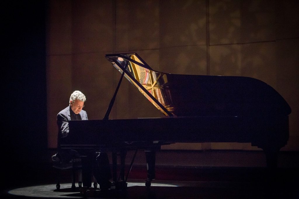 Pianista Homero Francesch tocando en escena iluminada, concentrado ante el teclado del piano de cola durante