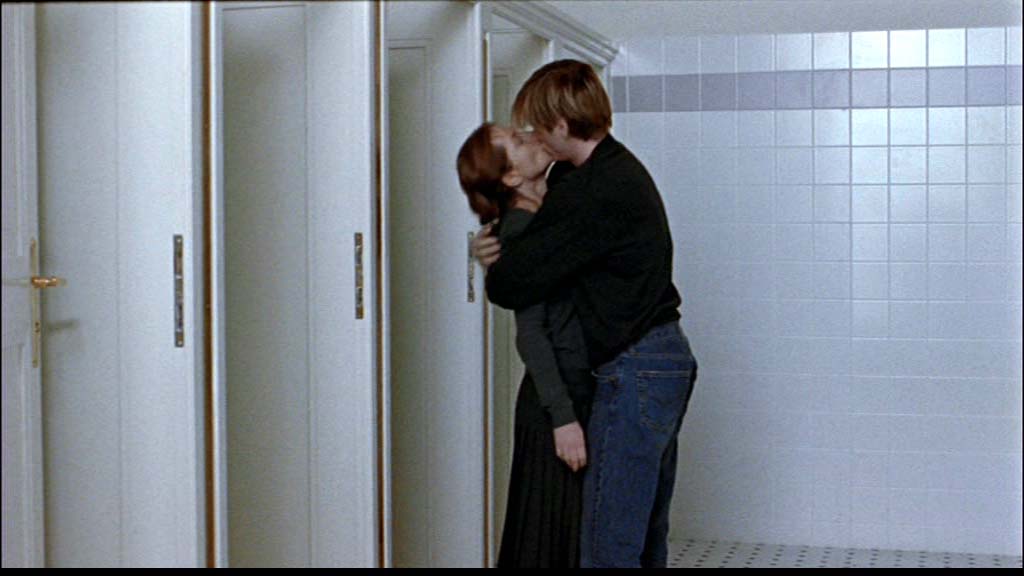 Pareja besándose en baño de azulejos blancos, escena íntima en espacio público minimalista