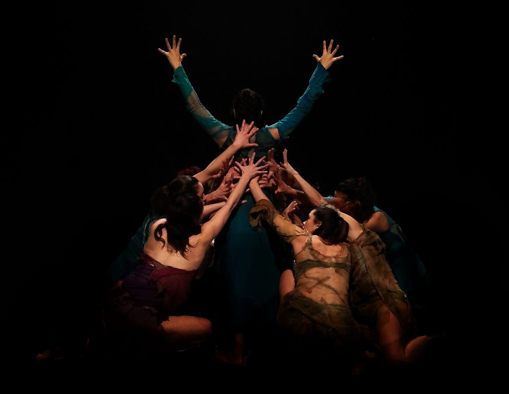 Tres figuras desnudas en escena oscura con brazos elevados, montaje teatral de Patricio Bunster