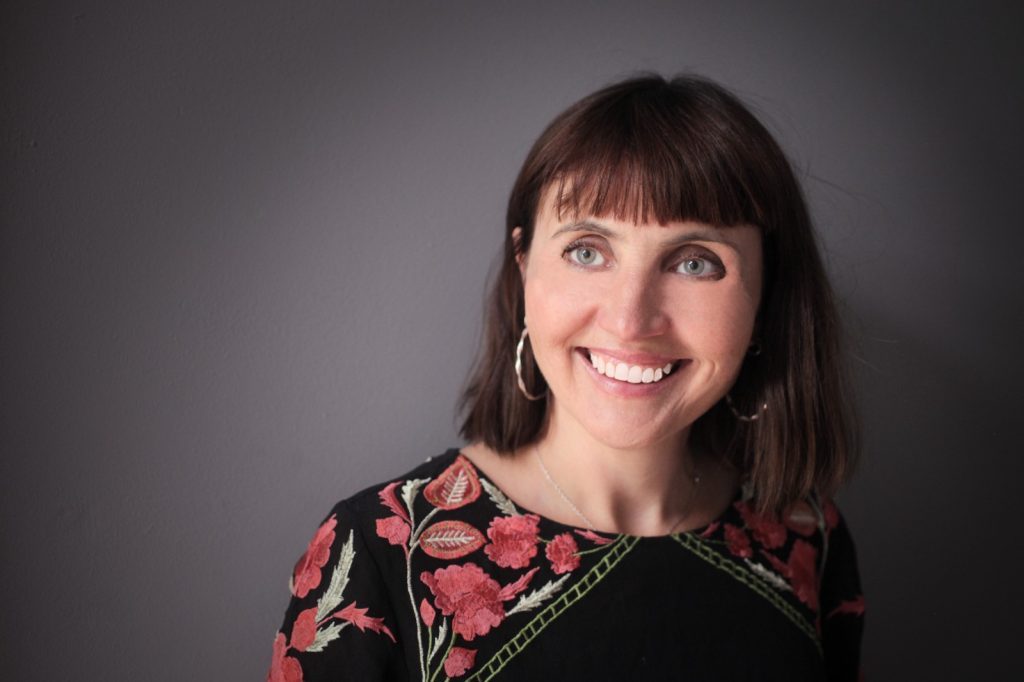 Novela "Our kind of cruelty", de Araminta Hall: El éxtasis de la tensión amorosa Retrato de Araminta Hall, autora, sonriendo ante fondo gris neutro con blusa estampada en tonos rojos y negros