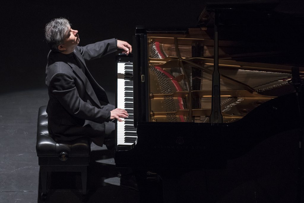Pianista Mario Alarcón al frente de un piano de cola en escenario oscuro durante presentación musical