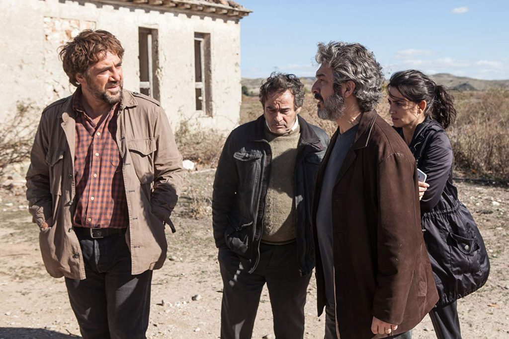 Cuatro actores en un camino frente a una casa de adobe en zona rural, en escena de tensión dramática