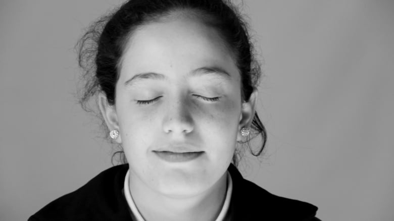 Documental "Acá y acullá", de Hernán Khourian: El silencio del genocidio armenio en imágenes Mujer con los ojos cerrados, expresión serena, cabello oscuro recogido, pendientes visibles, fondo gris neutro