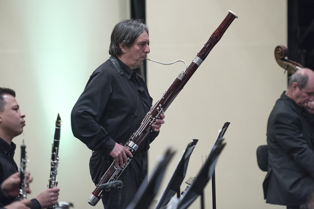 Músico toca fagot en concierto de la Orquesta Sinfónica Nacional de Chile, con otros instrumentistas de viento al fondo
