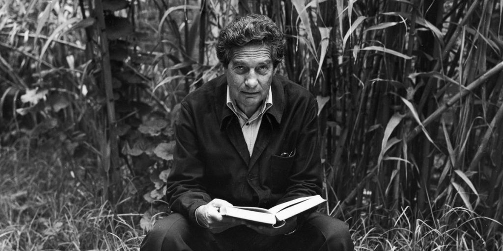 Versión teatral de "La hija de Rapaccini": El arte de la seducción, según Octavio Paz Octavio Paz sostiene un libro abierto, sentado entre plantas secas en fotografía en blanco y negro