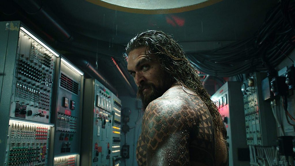 "Aquaman": La vigencia del cine de matiné Hombre con tatuajes en un traje mojado dentro de una sala de control tecnológica con paneles iluminados