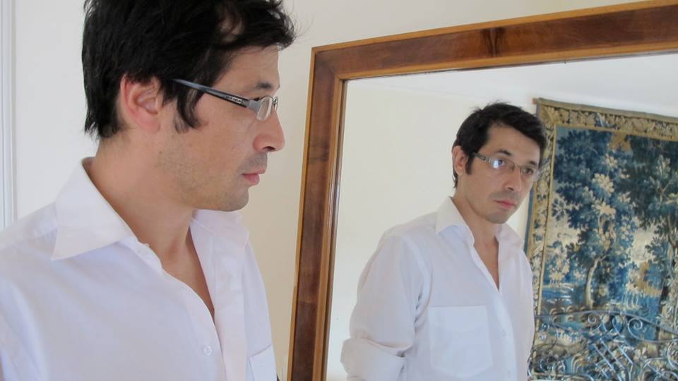 Germán Carrasco frente a un espejo, de perfil, vistiendo camisa blanca y lentes