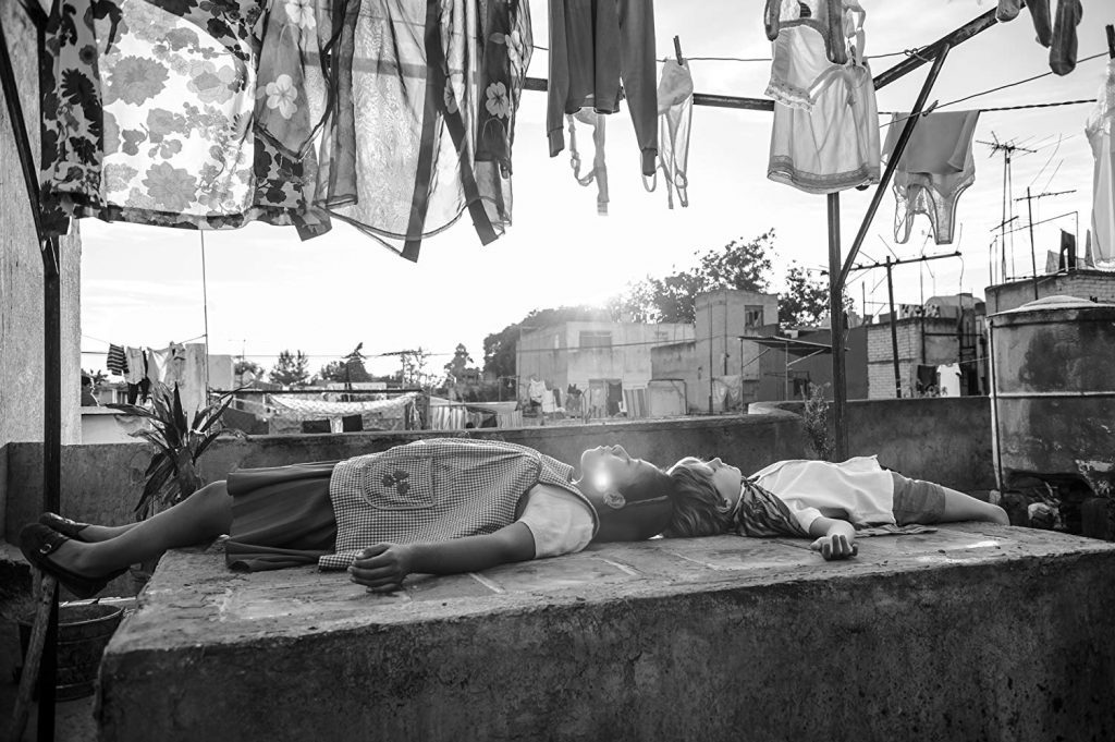 Hombre recostado sobre superficie de concreto en azotea urbana con ropa tendida y ciudad de fondo