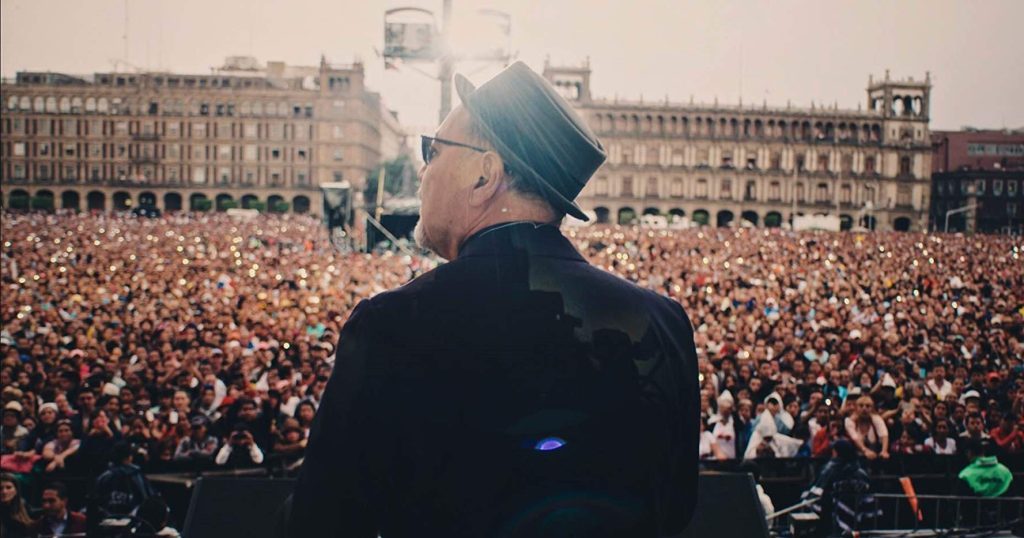 Documental "Yo no me llamo Rubén Blades": La voz de un ícono latinoamericano Rubén Blades de espaldas frente a multitud en plaza pública, vistiendo abrigo oscuro y gorro azul