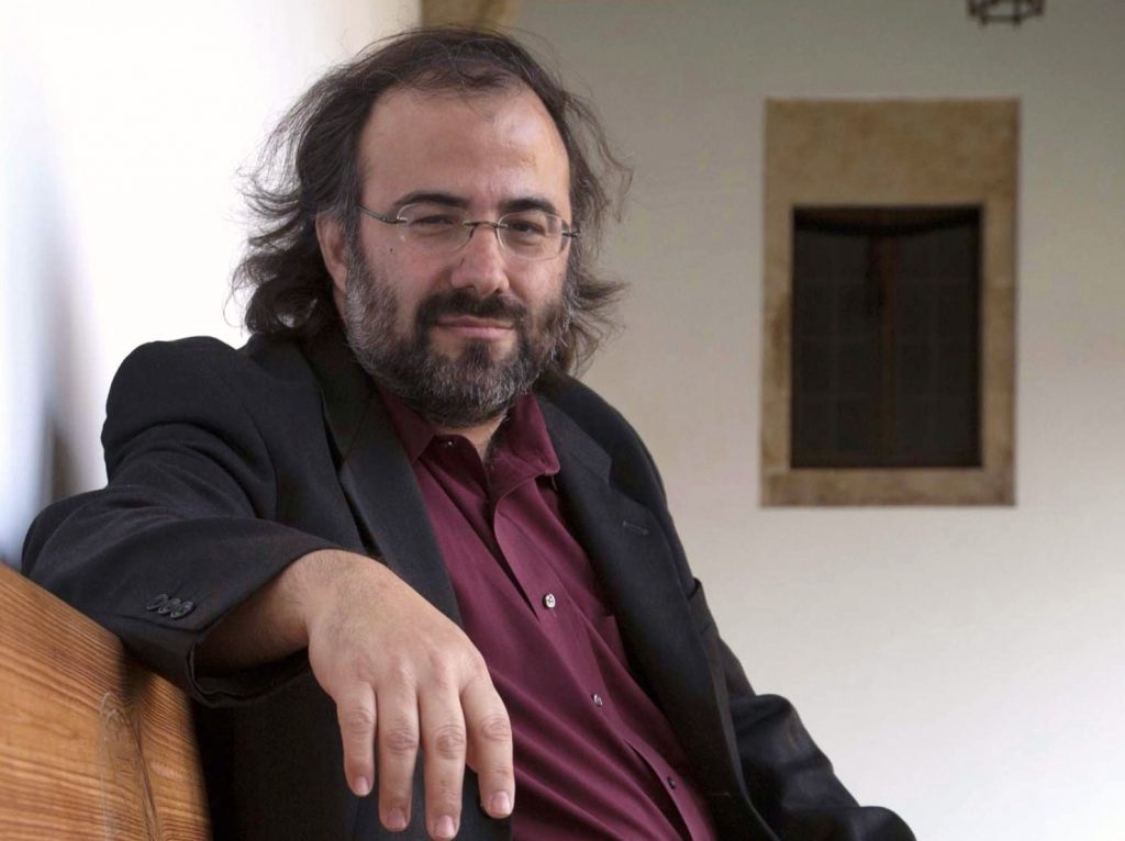 Alfredo Pérez Alencart, poeta y escritor, posando en interior blanco con blazer negro y camisa vino
