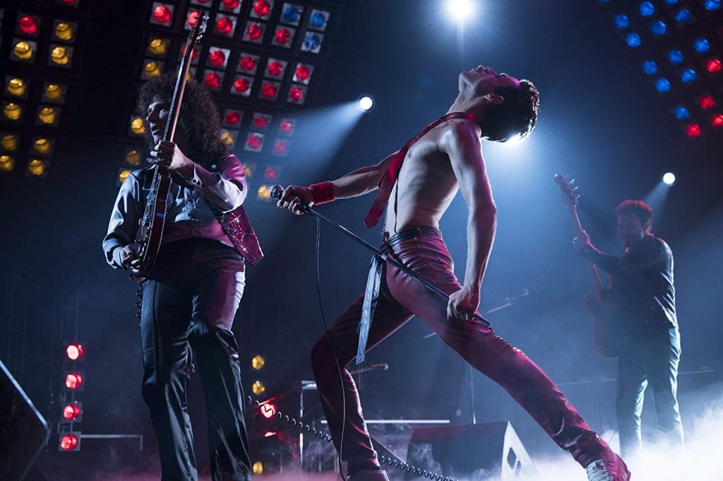 "Bohemian Rhapsody": La mística de Freddie Mercury y de Queen Freddie Mercury sin camisa en escena de concierto, tocando micrófono frente a guitarrista y luces de escenario coloridas