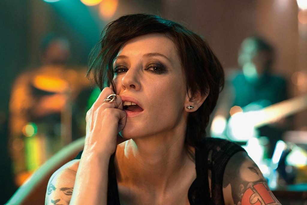 Mujer con tatuaje en el brazo, mano cerca del rostro, expresión pensativa en ambiente de concierto o estudio con luces