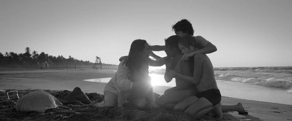 Dos mujeres sentadas en la playa al atardecer en blanco y negro, con el mar y la costa de fondo