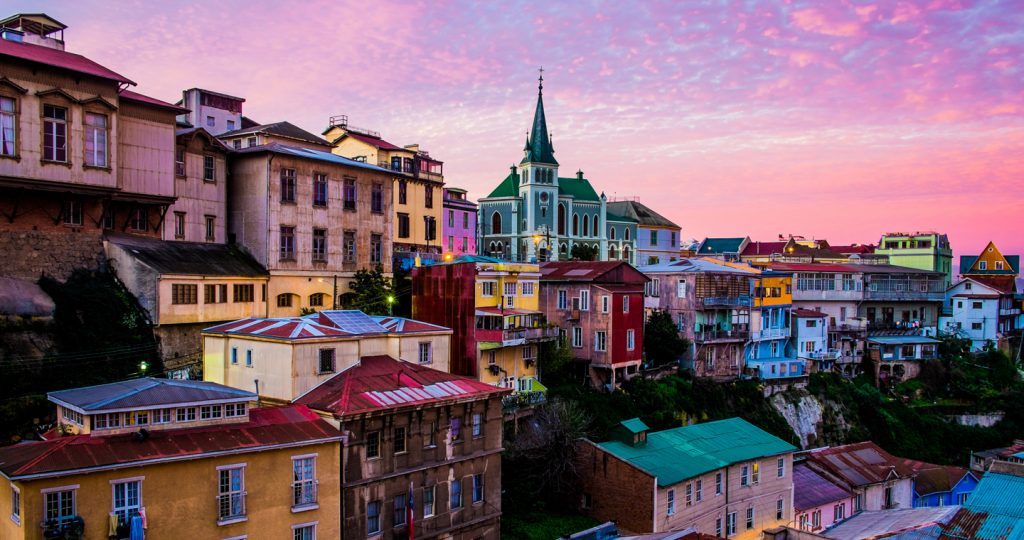 Casas coloridas en las laderas de Valparaíso al atardecer, con iglesia de torre verde y cielo rosado
