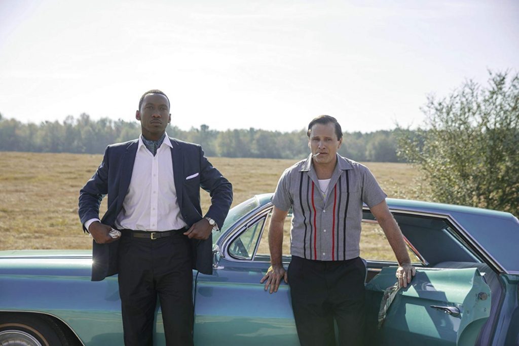 Dos hombres junto a un automóvil azul clásico en una carretera rural, escena de la película Green Book
