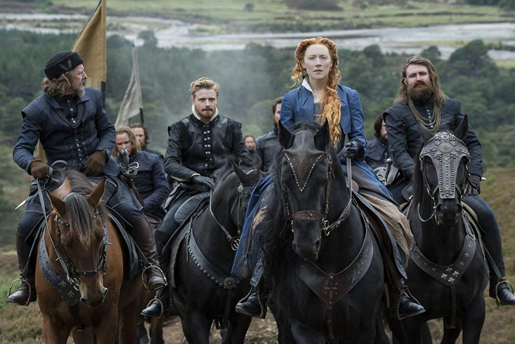 Cinco personas a caballo en paisaje montañoso, vistiendo ropas medievales oscuras, en escena de drama histórico