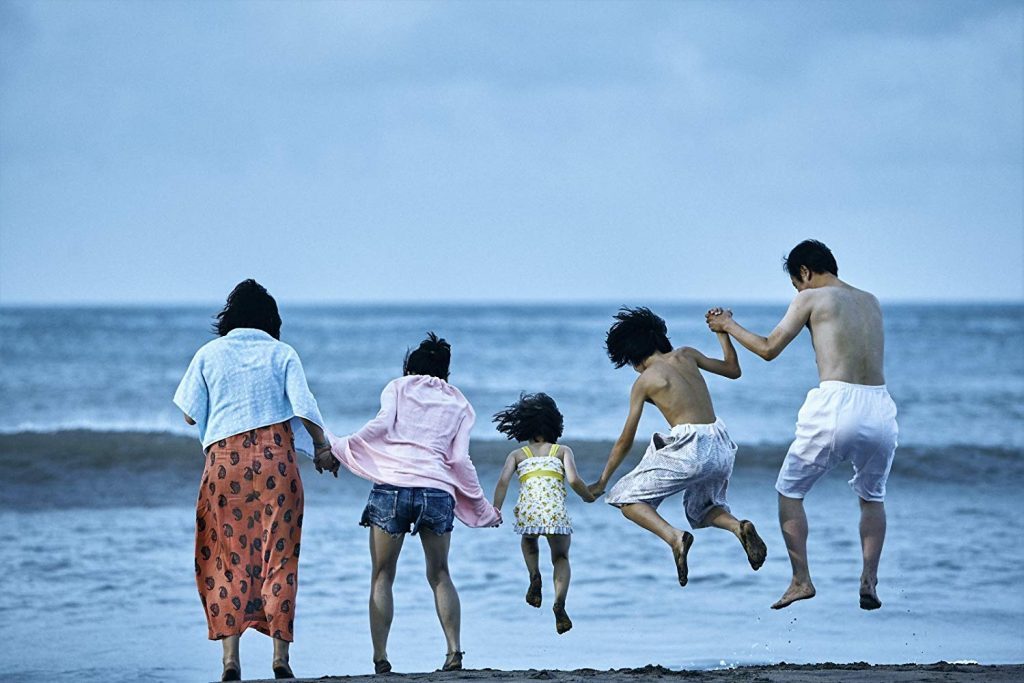 Familia corriendo hacia el mar en la playa durante el día, con adultos y niños tomados de las manos en actitud