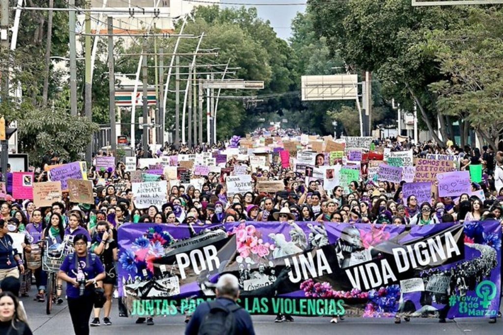 Multitud de personas en marcha callejera sosteniendo pancartas moradas y carteles con consignas feministas