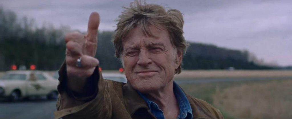 Robert Redford sonríe y levanta la mano en gesto de paz en una escena campestre