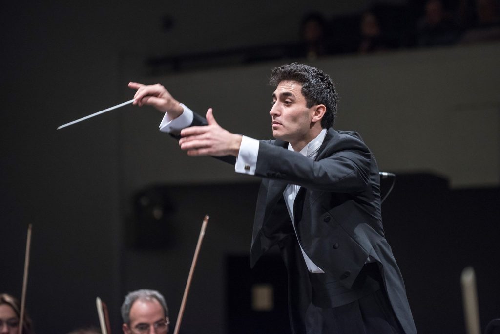 Director de orquesta en traje oscuro levantando la batuta durante una presentación de la Orquesta Sinfónica Nacional
