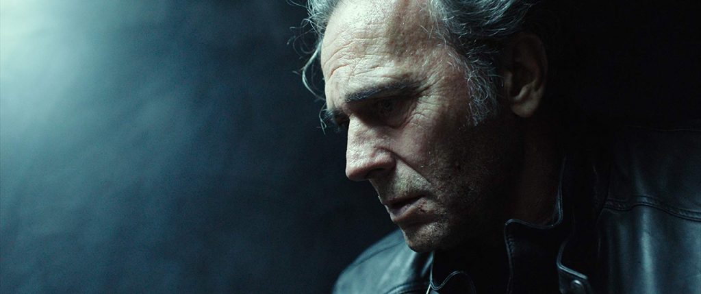 Hombre de mediana edad con expresión seria en primer plano, iluminación dramática azul, ambiente oscuro y tenso