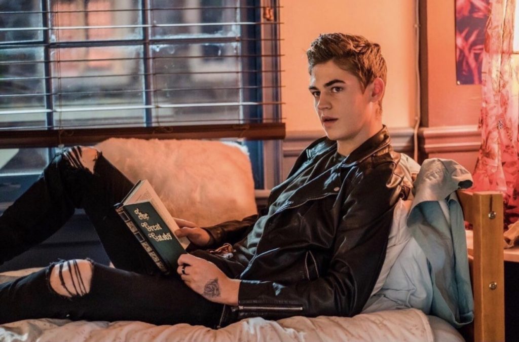 "After": Cuidado con los estereotipos Joven con cabello rubio en chaqueta de cuero negra, recostado en sofá beige, sosteniendo libro en habitación naranja