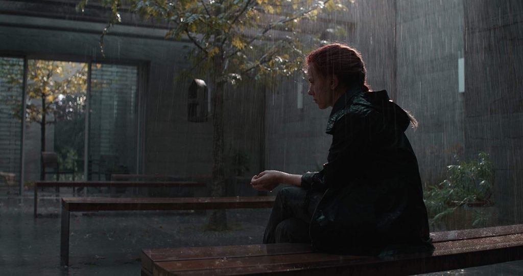 "Avengers: Endgame": La pantalla sagrada Hombre de cabello oscuro sentado en banco de madera, mirando hacia una pantalla iluminada en ambiente oscuro y lluvioso