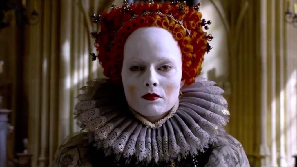 "Dos reinas": La seducción histórica de la intransigencia Mujer con peluca roja rizada y maquillaje blanco intenso, viste elaborado traje isabelino con cuello plisado gris