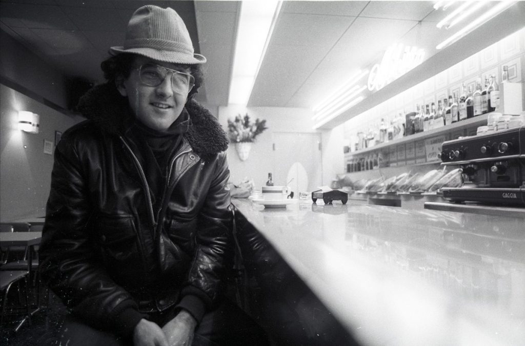 Roberto Bolaño sonriendo en el interior de un bar, vistiendo sombrero y chaqueta de cuero negra
