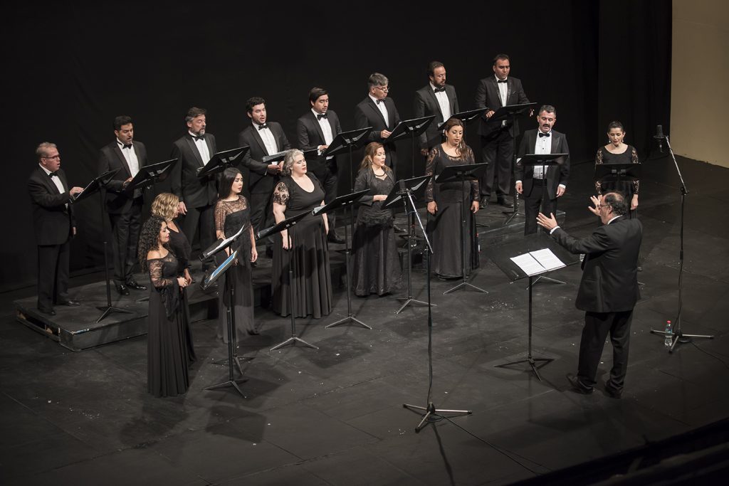 Camerata Vocal de la Universidad de Chile en formación coral sobre escenario, con director frente al grupo