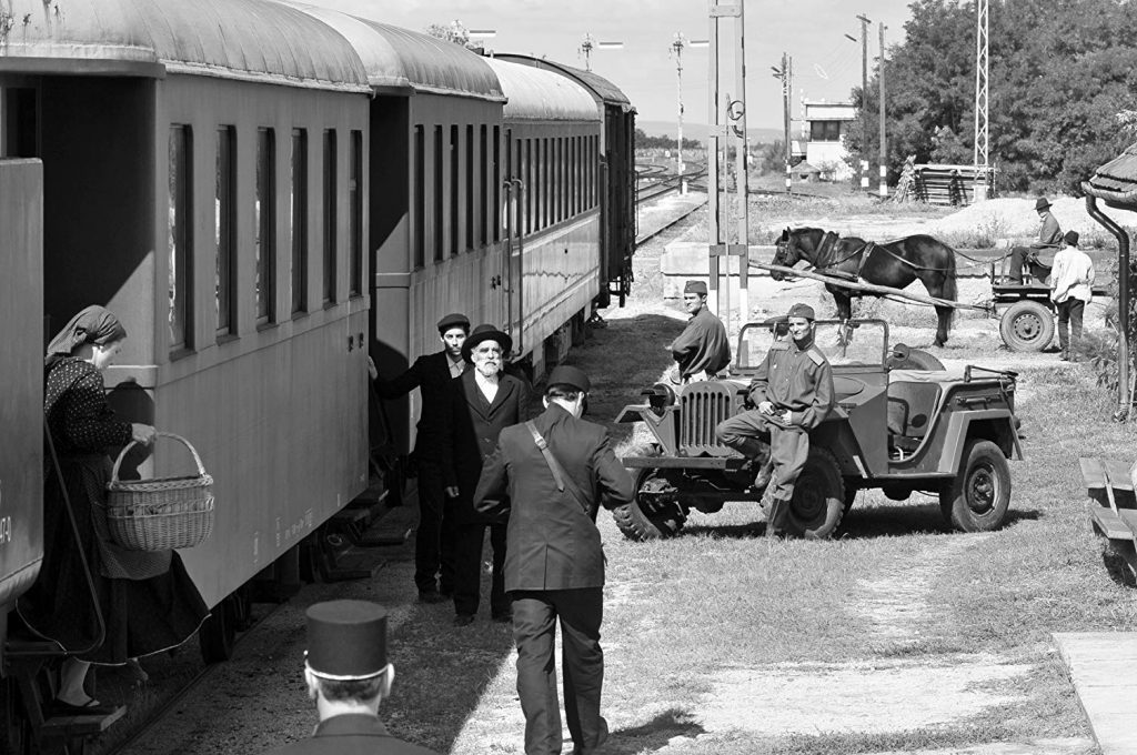 Escena de 1945 con personas bajando de un tren mientras otras esperan en la estación con equipaje y vehículos