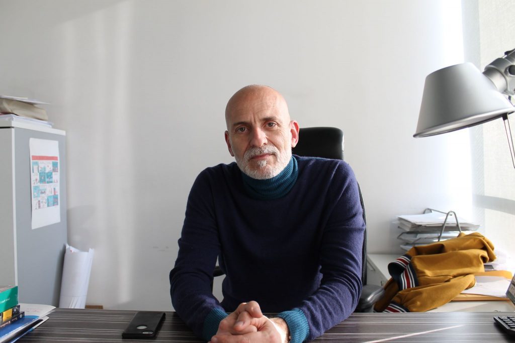 Alejandro Palomas, autor español, sentado en su escritorio con gafas, rodeado de libros y material de trabajo