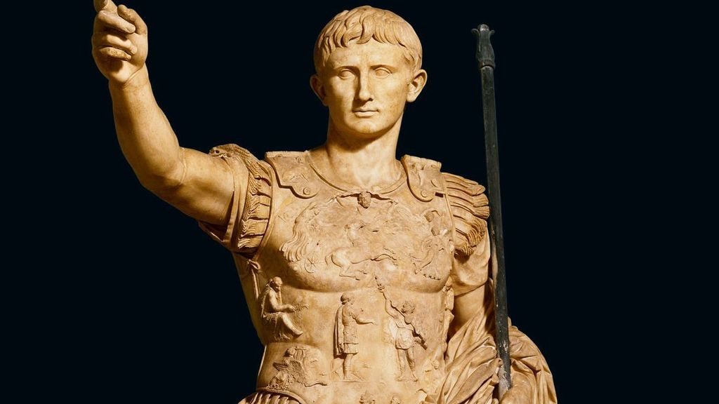 Estatua de mármol del emperador Augusto con brazo levantado en gesto de autoridad, vistiendo armadura romana decorada