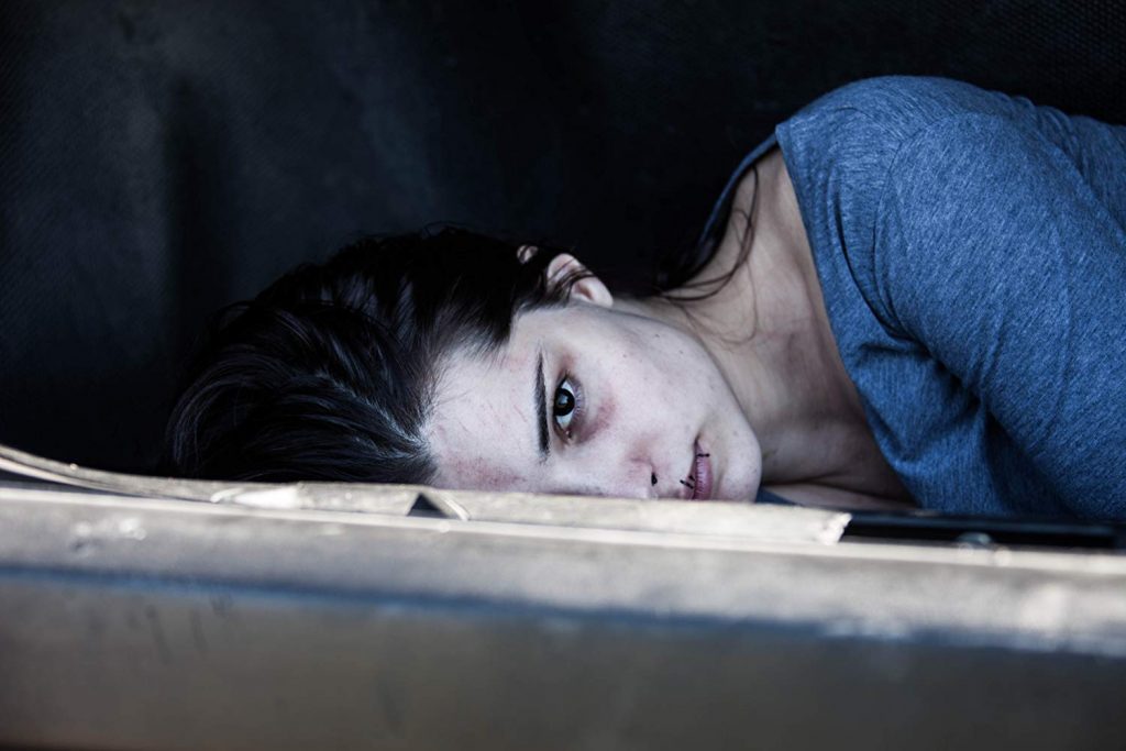 Mujer recostada en el suelo con expresión de angustia, vestida de azul, en escena de drama cinematográfico