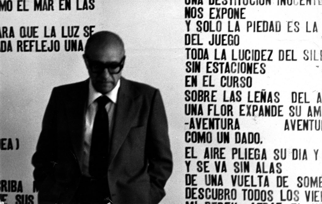 Godofredo Iommi, escritor chileno, con gafas oscuras en primer plano, junto a textos literarios en blanco y negro