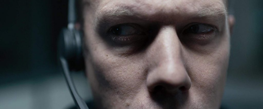Hombre con auriculares, expresión tensa y mirada angustiada en primer plano, bajo iluminación oscura y cinematográfica