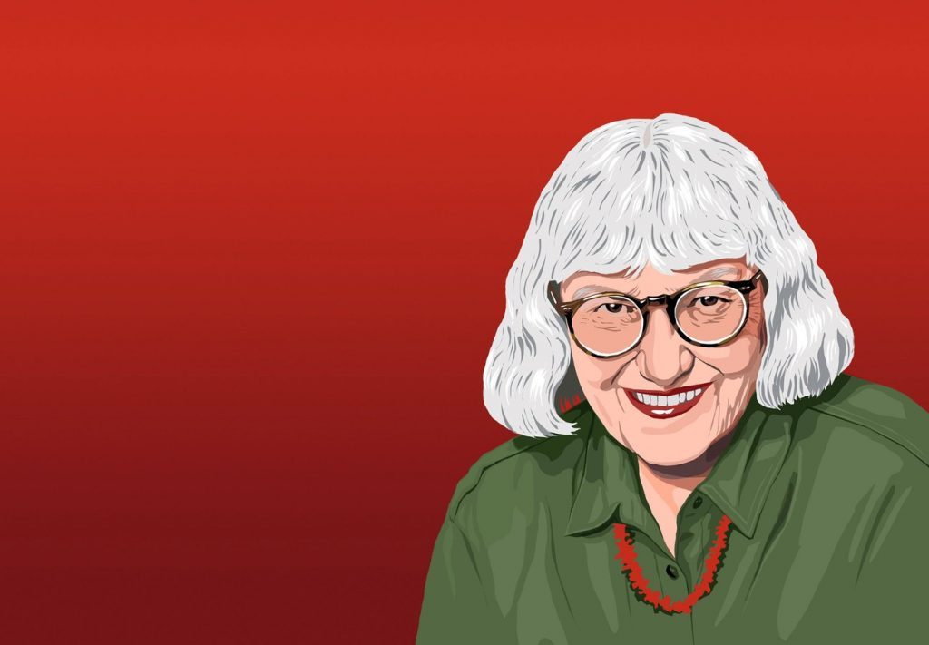 Cynthia Ozick, escritora con cabello blanco y gafas, sonriendo ante fondo rojo