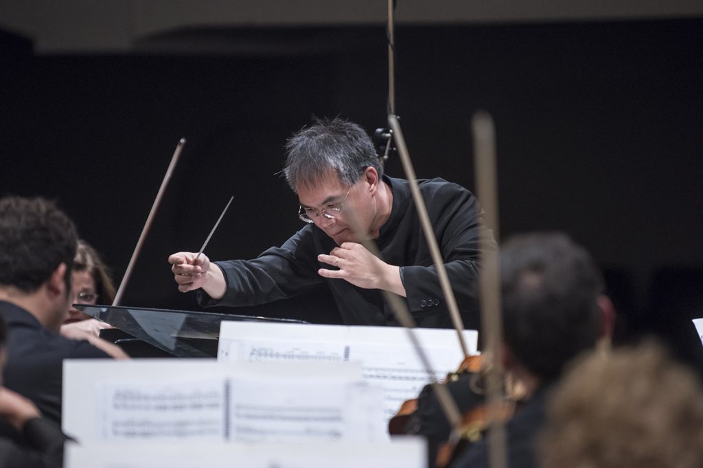 Director de orquesta con batuta dirige a músicos durante ensayo o concierto de música clásica sinfónica