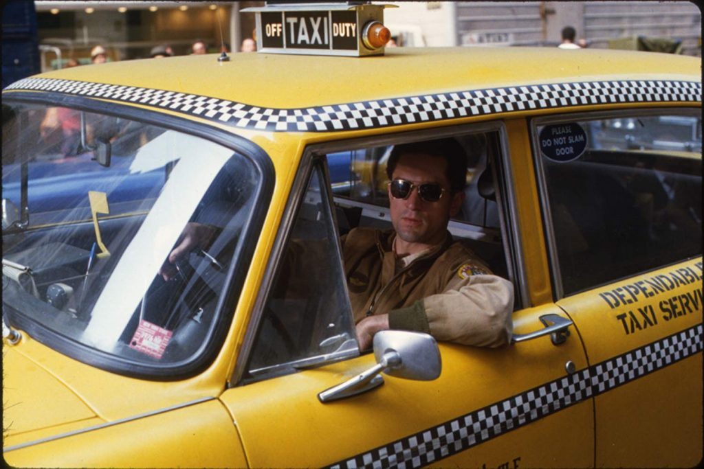 Hombre con gafas de sol conduciendo un taxi amarillo con cuadros blancos y negros en la ciudad