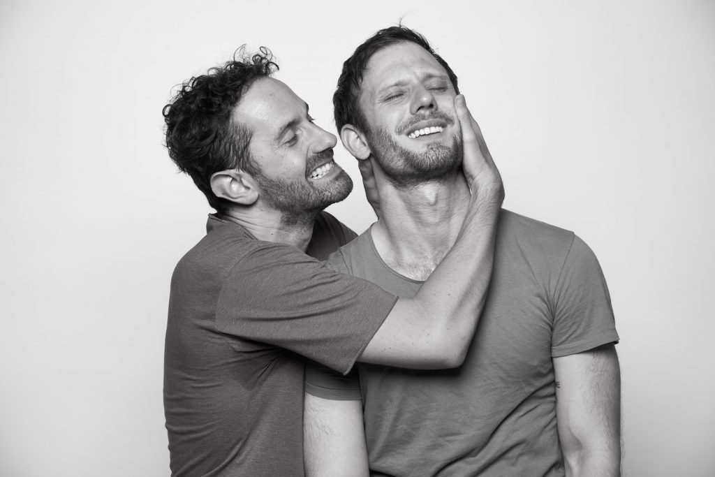 “Y un día Nico se fue…”: Una comedia musical en clave romántica Dos hombres jóvenes en camiseta gris en fotografía blanco y negro, uno abraza al otro por detrás en actitud cariñosa