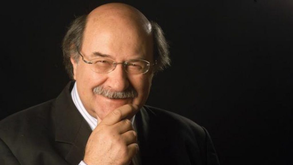 "Los nombres de las cosas que allí había", de Antonio Skármeta: Soñé que Chile ardía Antonio Skármeta, escritor chileno, retratado en primer plano con gafas y expresión reflexiva contra fondo negro