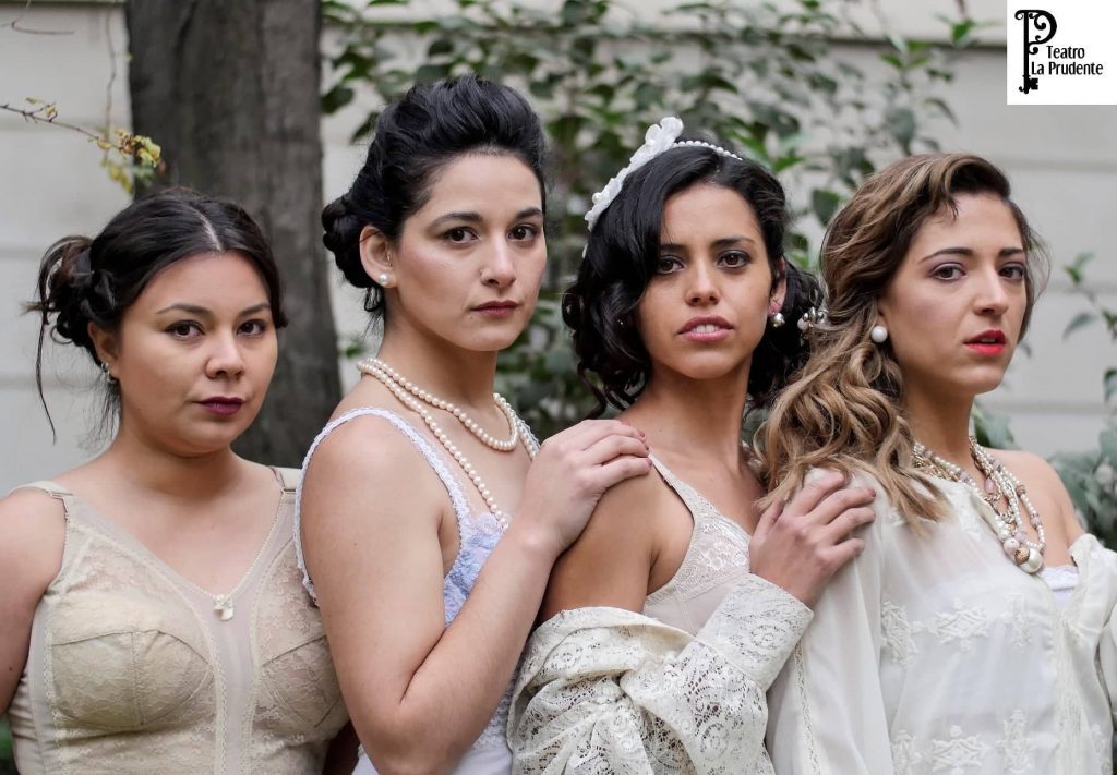 Cuatro mujeres jóvenes en vestidos blancos y claros posan juntas en un ambiente exterior con vegetación de fondo
