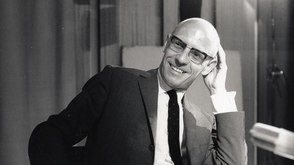 ¿Está todo dicho?: La postmodernidad en contra del proyecto humanista Michel Foucault, filósofo francés, retratado en blanco y negro con gafas y traje oscuro, apoyado en su mano