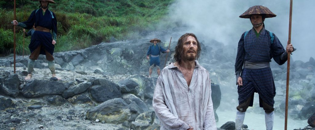 Sacerdote en blanco rodeado de samurais en paisaje rocoso durante escena de persecución religiosa en la historia de fe