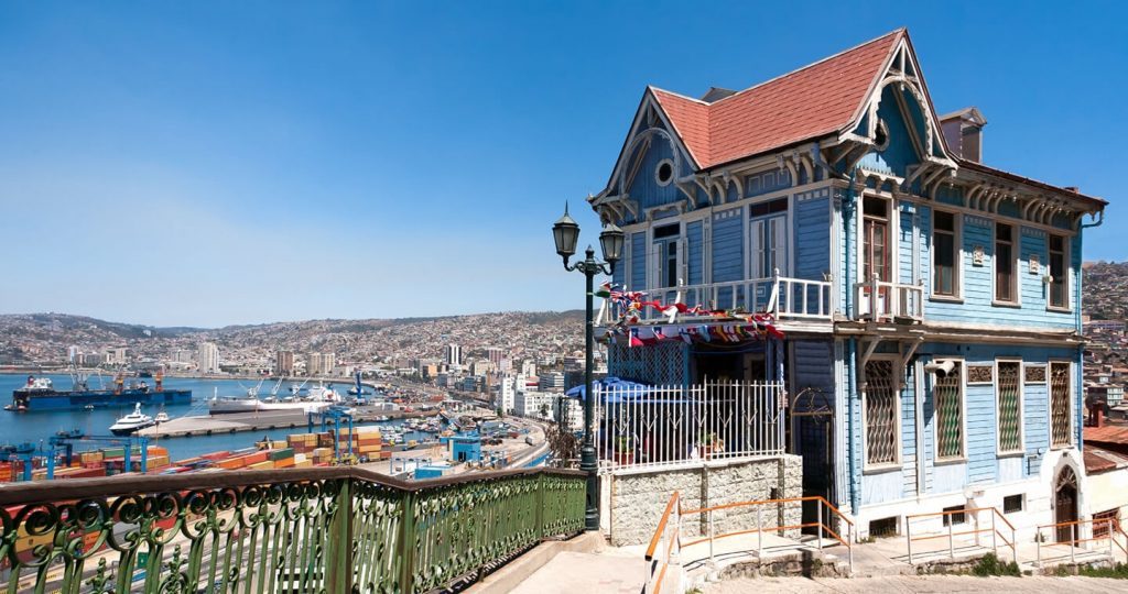 Casa victoriana blanca y azul en cerro de Valparaíso con vista al puerto y bahía al fondo bajo cielo despejado